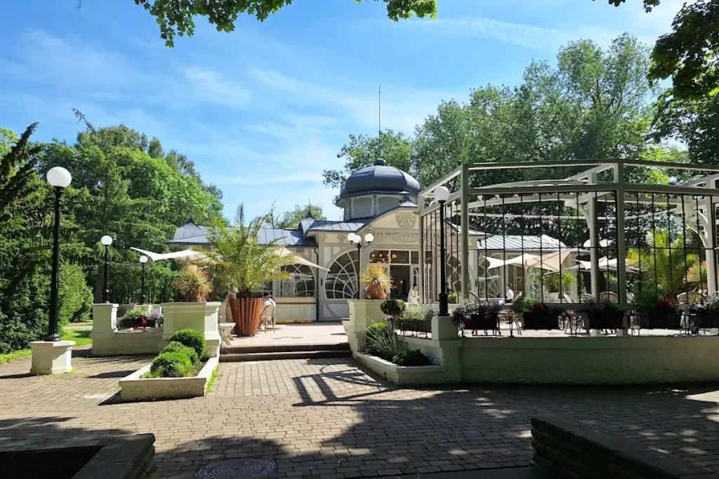 Café terrace surrounded by trees and landscaped gardens in Jūrmalas Park near Liepāja beach.
