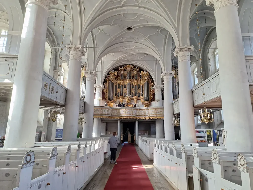 Holy Trinity Cathedral nave in Liepāja with white pews, red aisle carpet and the organ ahead